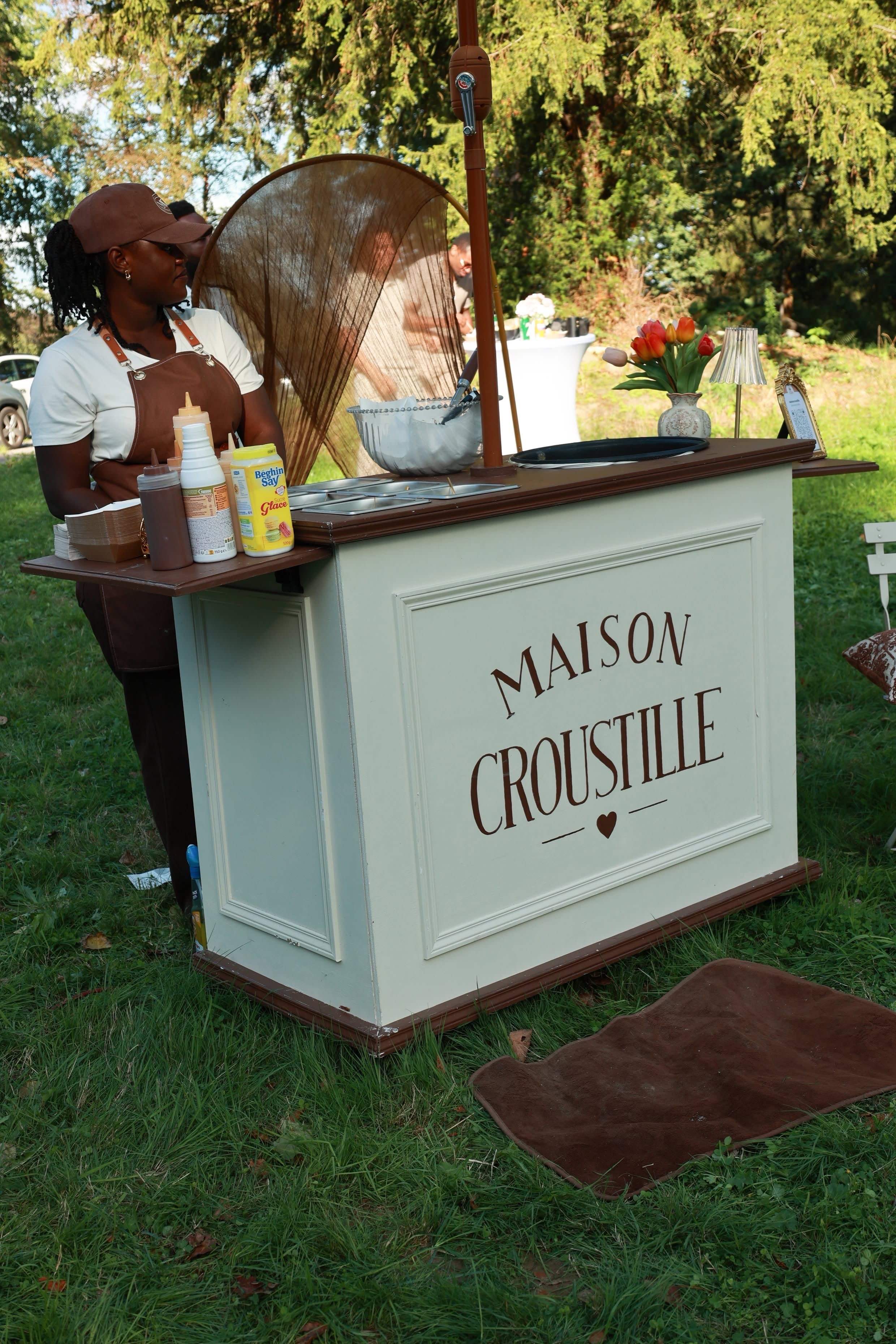 Une hôtesse Maison Croustille derrière le comptoir, installé sur la pelouse d’une réception en plein air.